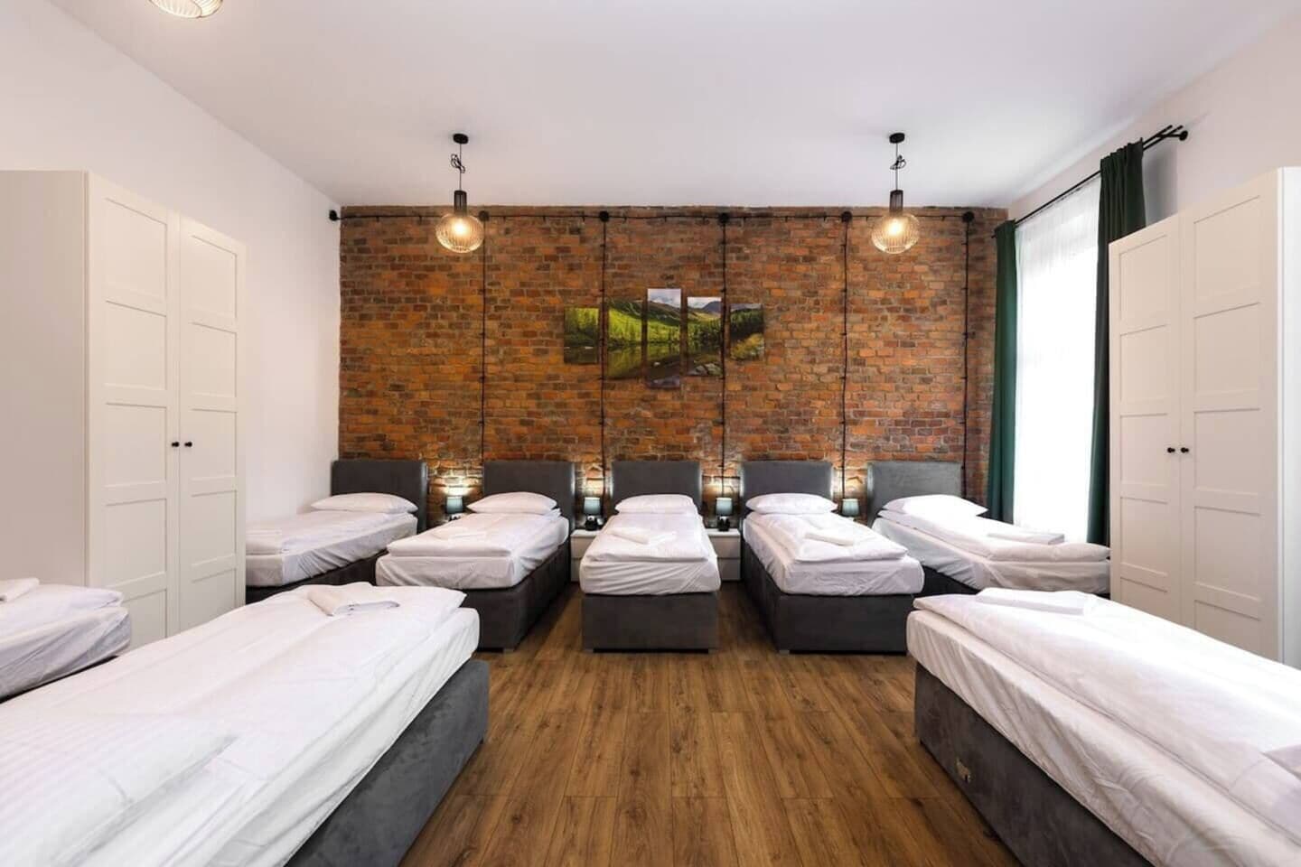 Una habitación de hotel con seis camas individuales, una pared de ladrillo y un ventanal grande.