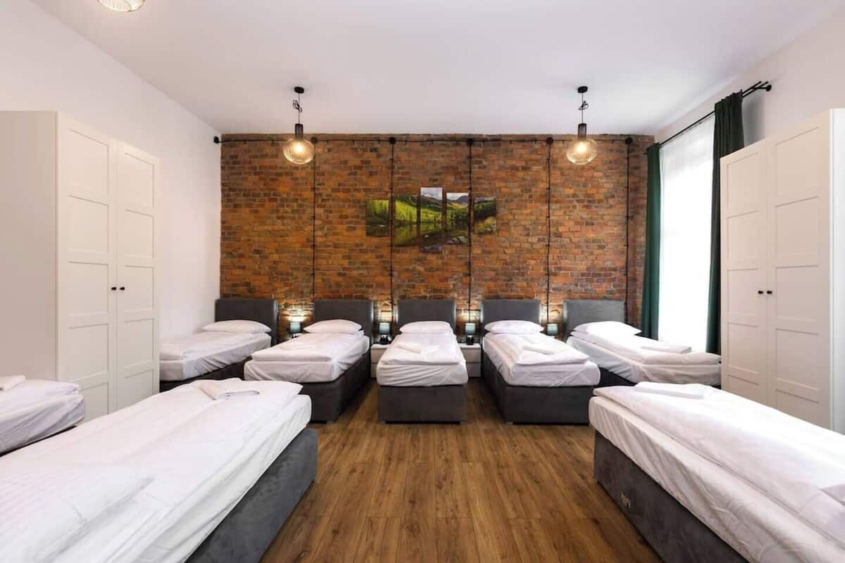 Una habitación de hotel con seis camas individuales, una pared de ladrillo y un ventanal grande.