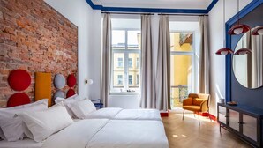 A hotel room with two beds, a brick wall, a large window with curtains, a blue accent wall, a red chair, and a black cabinet with a mirror. - SquadGoals House by Fragola Apartments (Kraków)
