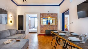A modern living room with a sofa, a dining table set for four, and a brick wall with a mirror. - SquadGoals House by Fragola Apartments (Kraków)
