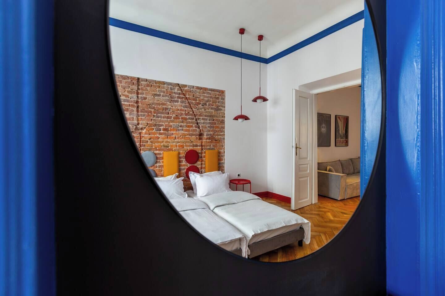 A bedroom with a brick wall, a bed with white bedding, red and yellow accent pillows, and a red pendant light.