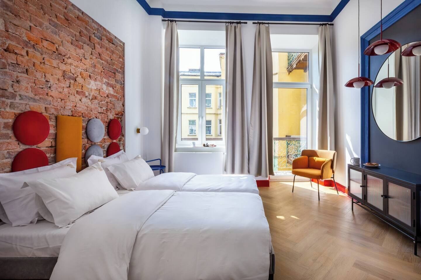 Una habitación de hotel con dos camas, una pared de ladrillo, un balcón y vistas a edificios.