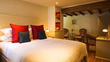 A hotel room with a large bed, red and black pillows, a wooden ceiling, and a seating area with chairs and a table.