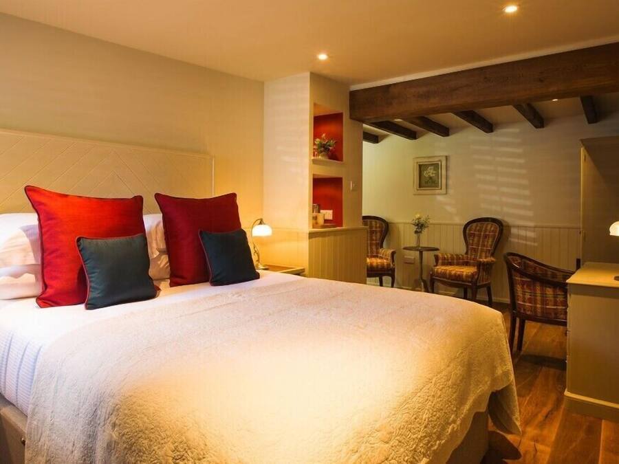 A hotel room with a large bed, red and black pillows, a wooden ceiling, and a seating area with chairs and a table.
