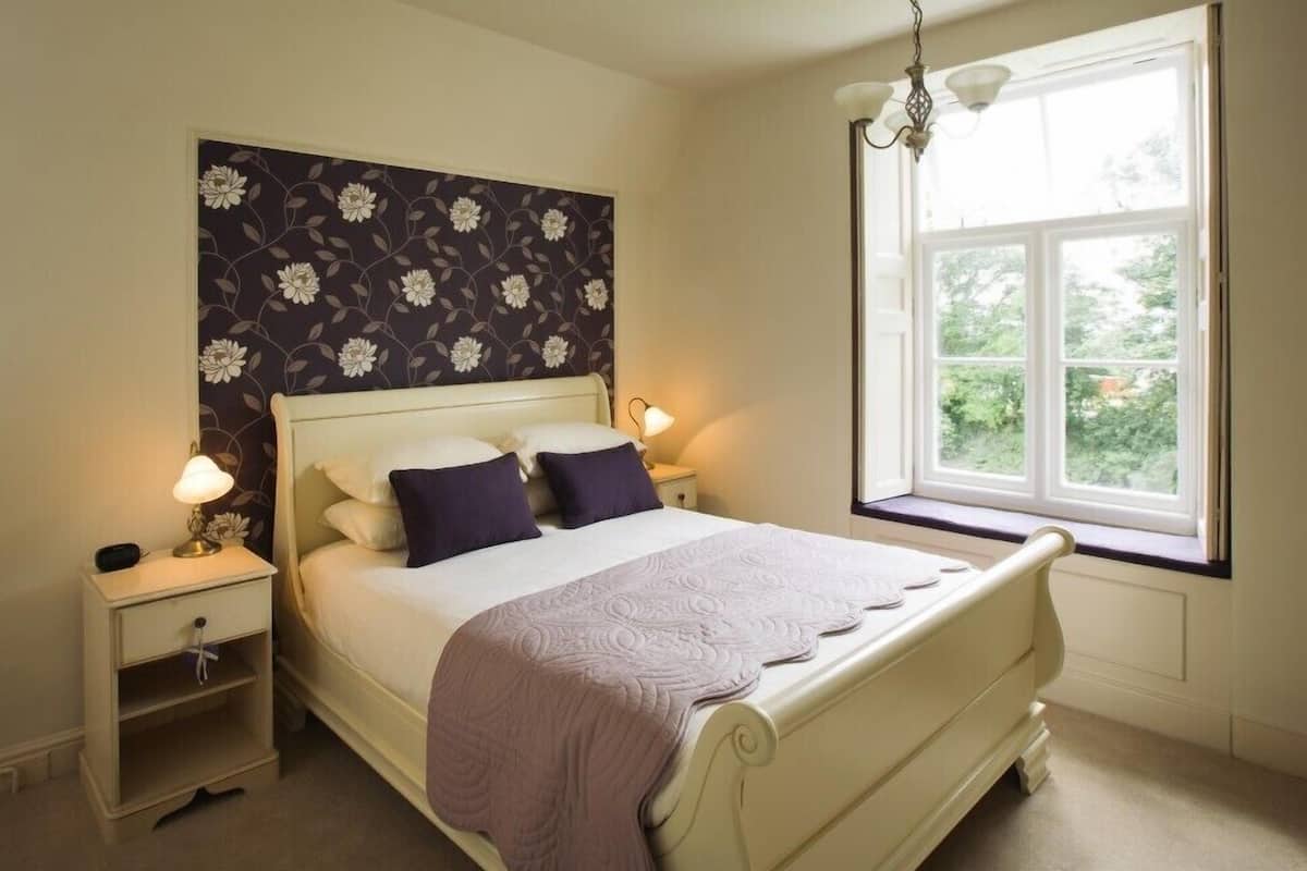 A bedroom with a bed, nightstands, a window, and a floral wallpaper.