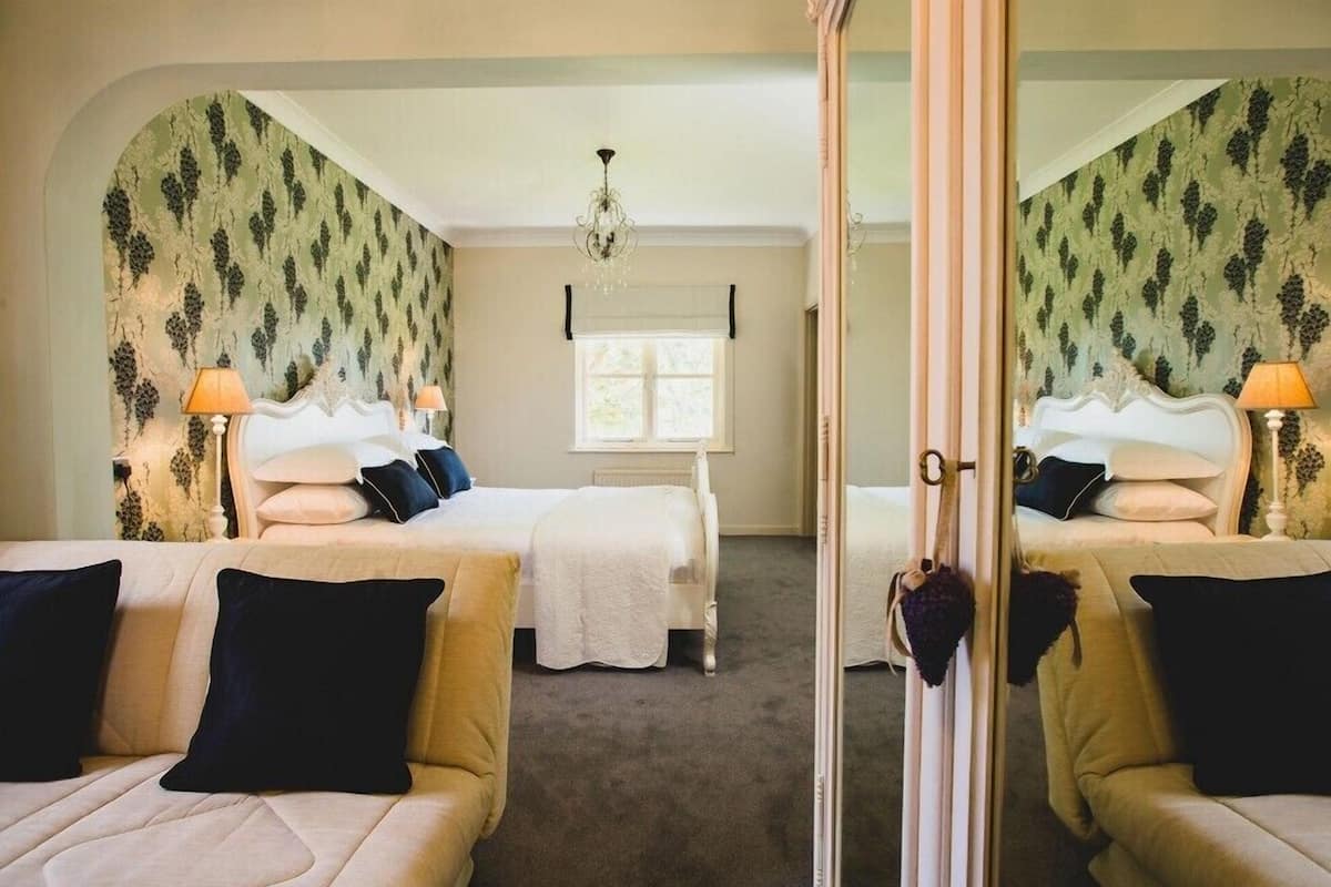 A mirrored room with two beds, a chandelier, and a window with blinds.