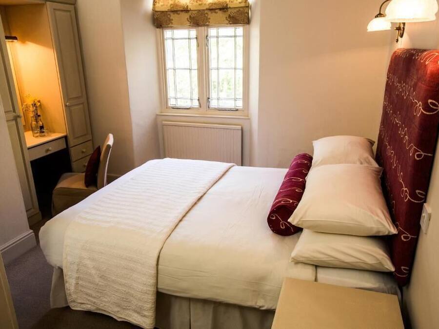 A neatly arranged bedroom with a bed, a bedside table, a window with curtains, and a wall-mounted lamp.