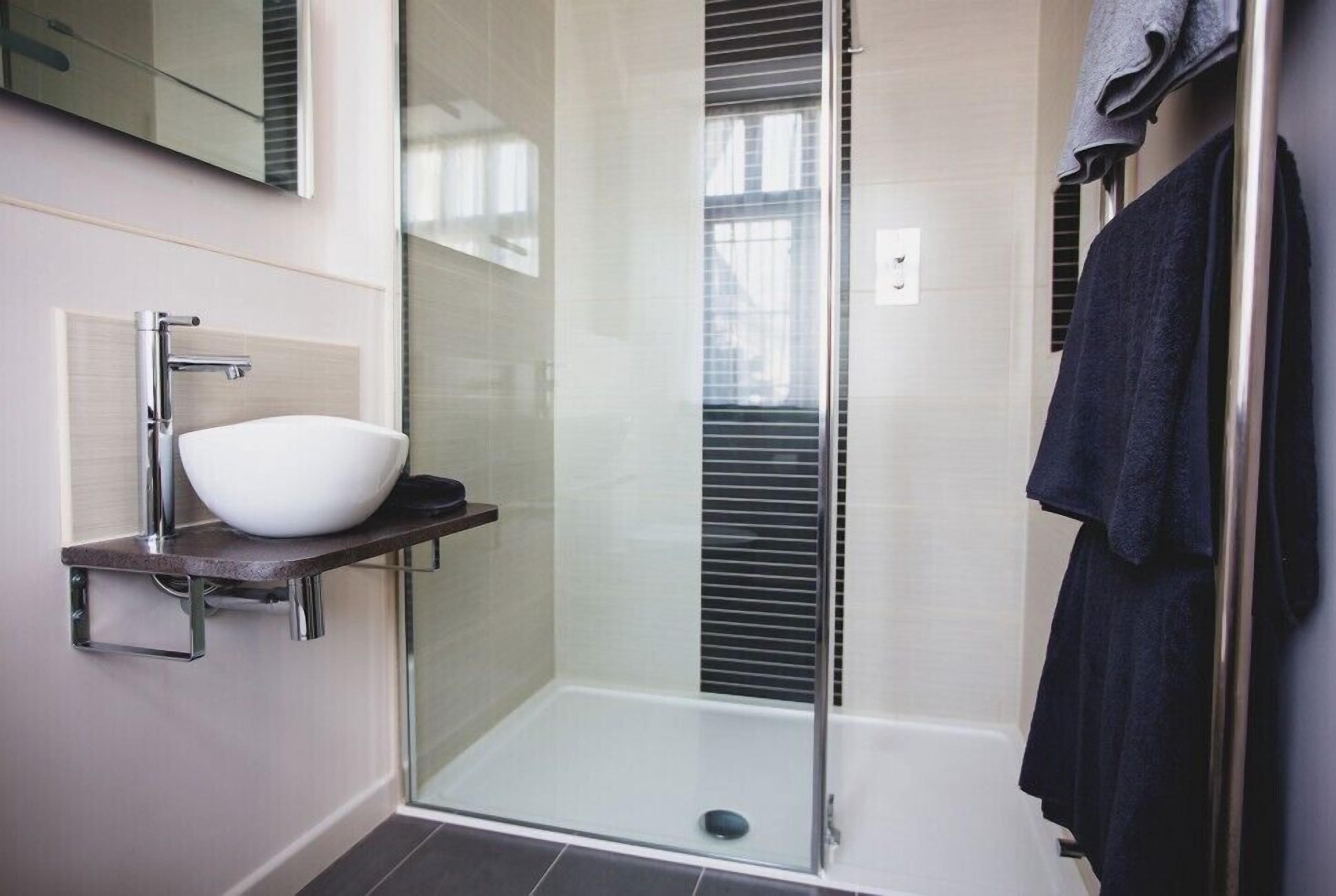 A modern bathroom with a glass shower enclosure, a white sink on a dark countertop, and a towel rack.