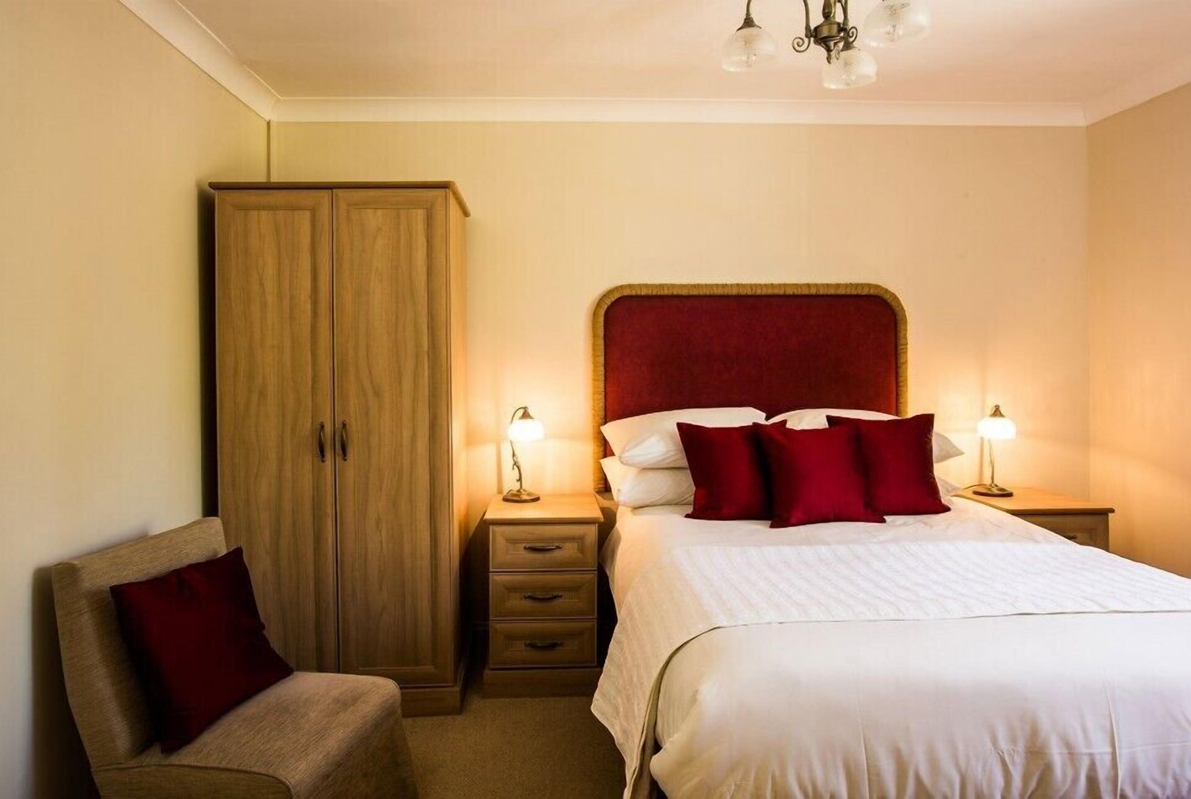A bedroom with a bed, two bedside tables with lamps, a wooden wardrobe, and a chair.