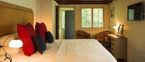 A bedroom with a bed, a nightstand with a lamp, a chair, a desk with a lamp, and a window with blinds.