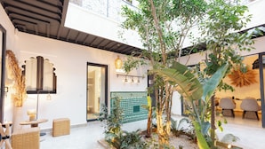 Un intérieur moderne avec un jardin central, des meubles en osier et un coin repas avec des chaises.