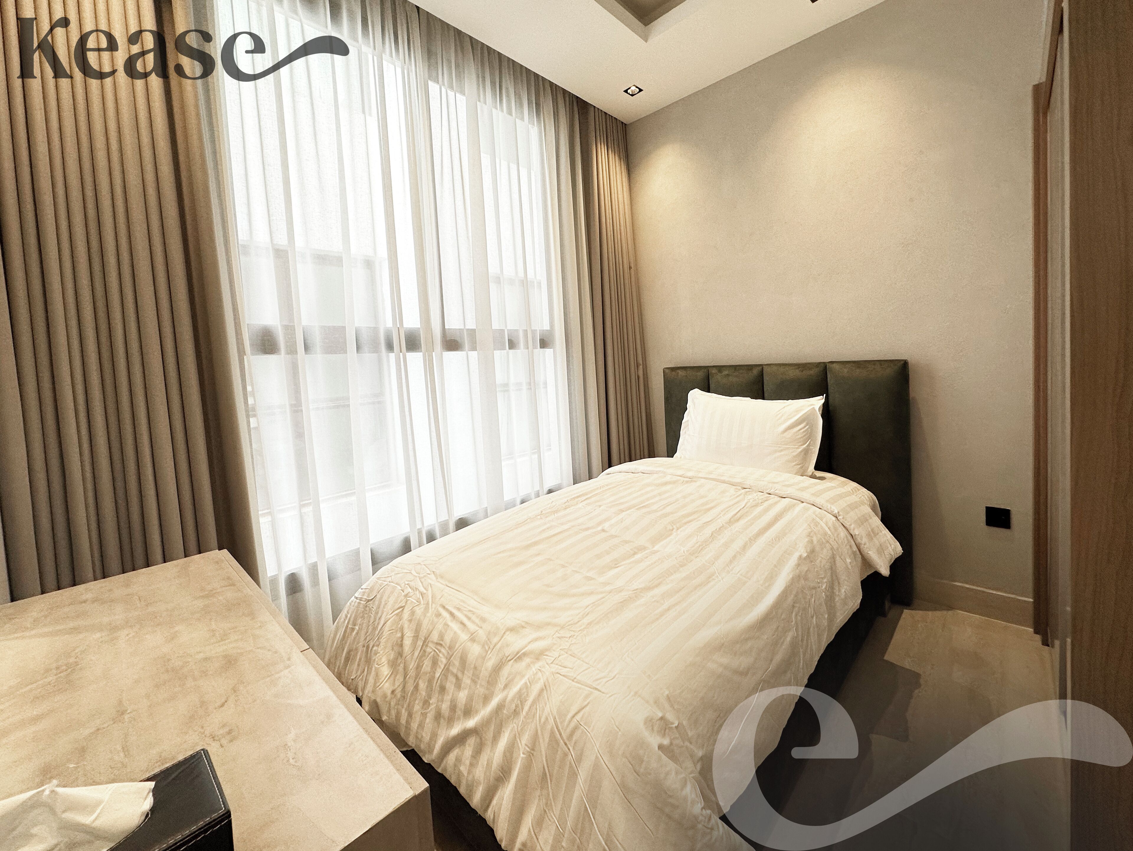 A hotel room with a bed, a bedside table, a window with curtains, and a headboard.