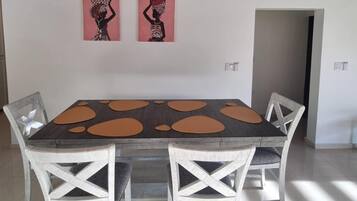 A dining area with a rectangular table, four white chairs, and two wall-mounted paintings.