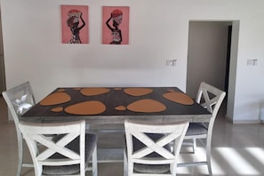 A dining area with a rectangular table, four white chairs, and two wall-mounted paintings.