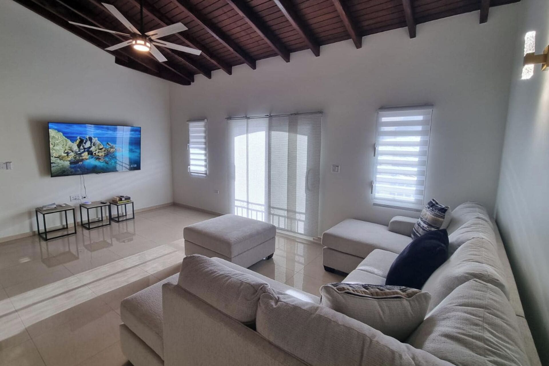 Ein geräumiges Wohnzimmer mit großem Flachbildfernseher, Deckenventilator und einem modernen Sofa.