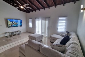 Een ruime woonkamer met een grote flatscreen-tv, een plafondventilator en een moderne bank.