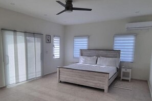Une chambre à coucher comprenant un lit, un ventilateur de plafond, une fenêtre et un appareil de climatisation.