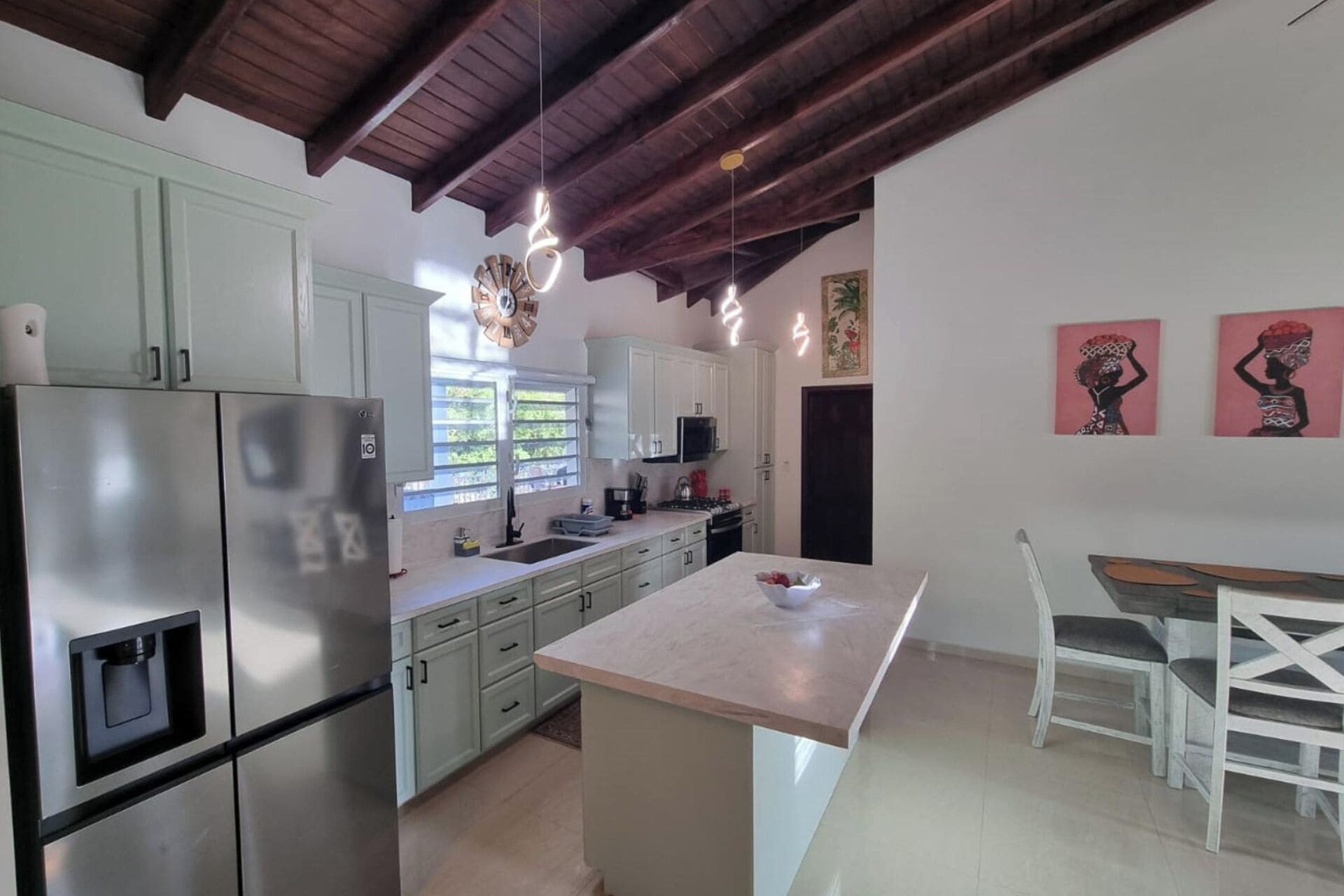 A modern kitchen with white cabinets, stainless steel appliances, and a central island. There is a dining area with a white table and chairs.