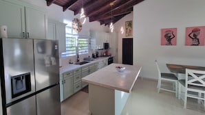 Una cocina moderna con armarios blancos, electrodomésticos de acero inoxidable y una isla central. Hay un comedor con una mesa y sillas blancas.