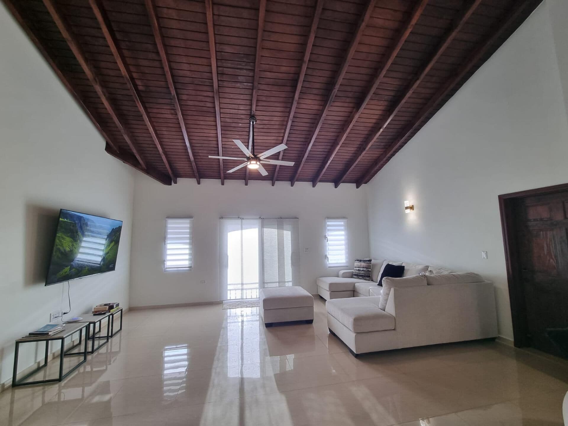 A spacious living room with a high ceiling, a ceiling fan, a flat-screen TV, a sofa, and a coffee table.