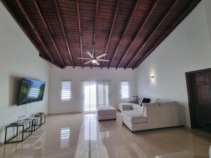 Un salon spacieux avec un plafond haut, un ventilateur de plafond, un téléviseur à écran plat, un canapé et une table basse.