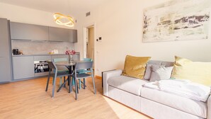 A modern kitchen with grey cabinets, a dining table with chairs, and a grey sofa with cushions. - Rosa dei Venti Est in Padenghe sul Garda (Padenghe sul Garda)