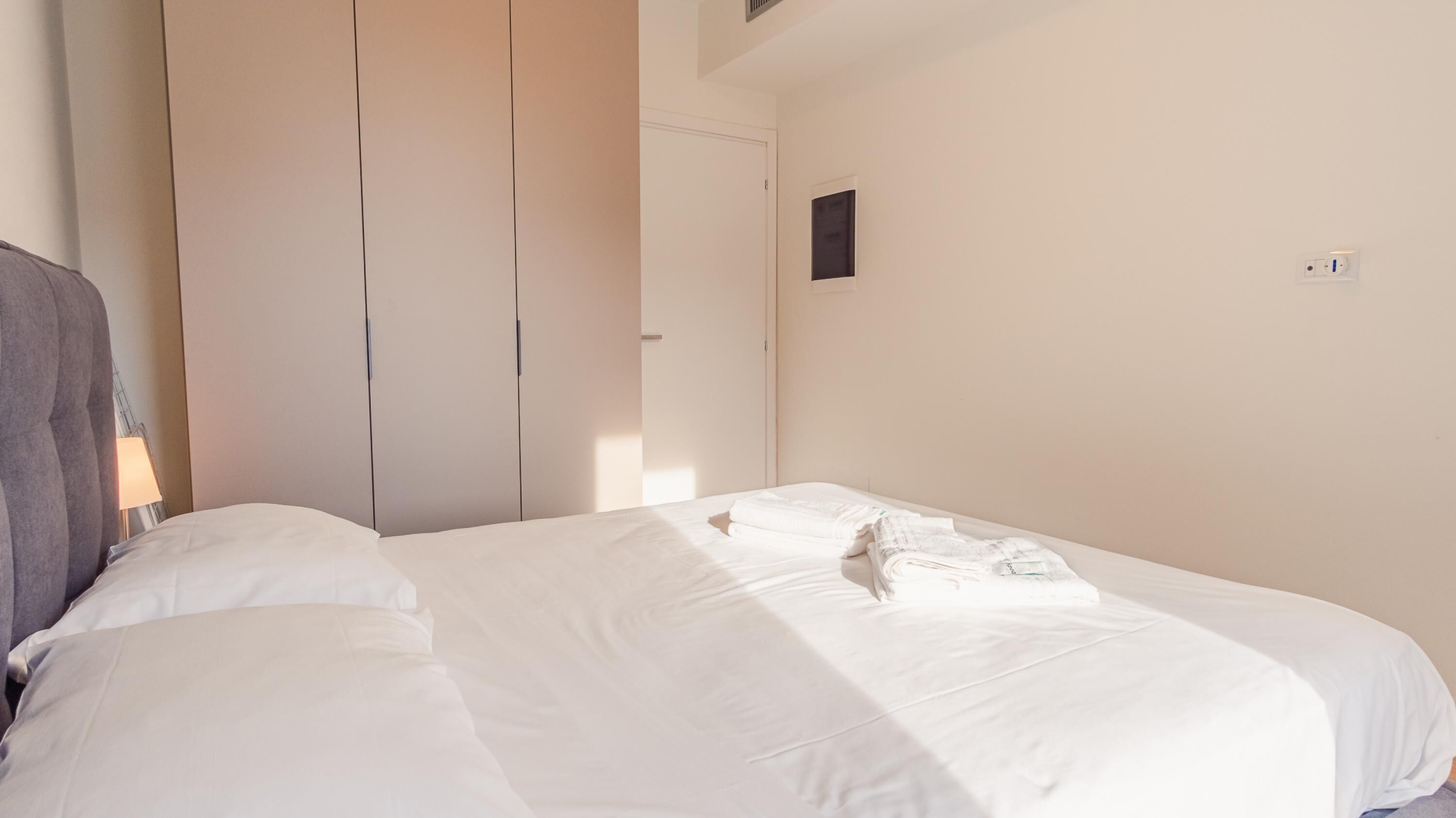 A hotel room with a bed, a wardrobe, and a small wall-mounted control panel.