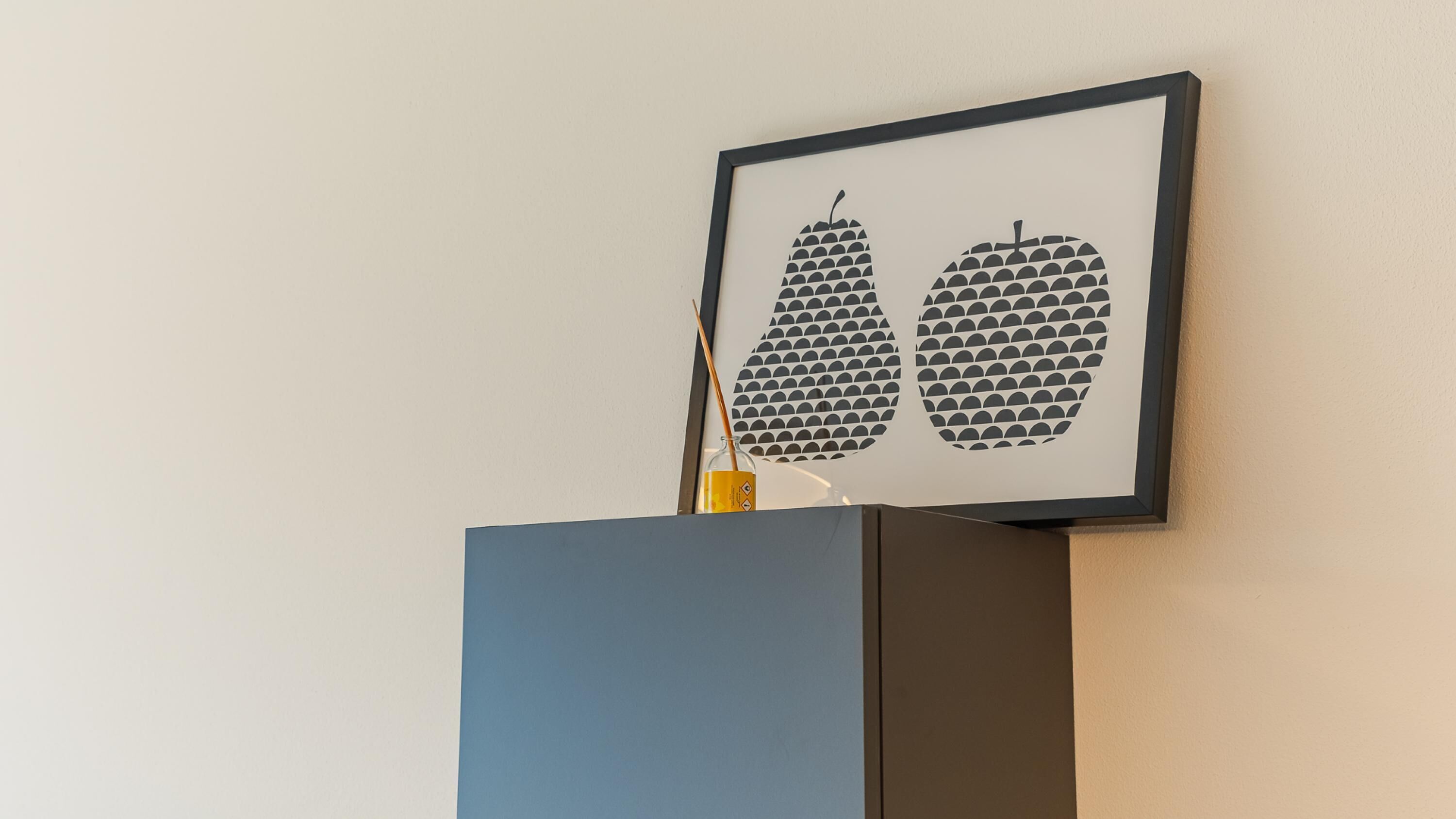 A framed artwork of two abstract apples on a wall.