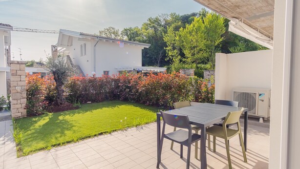 A patio with a table and chairs, a small lawn, and a white building in the background. - Rosa dei Venti in Padenghe sul Garda (Padenghe sul Garda)