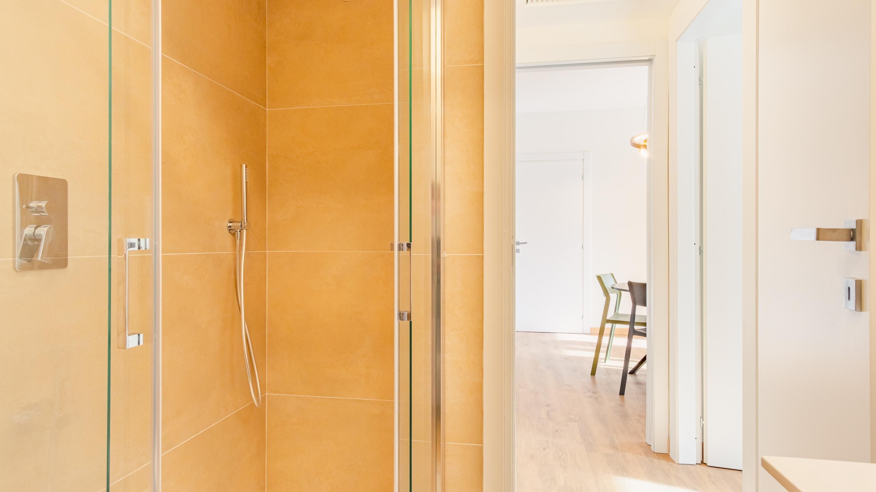 Een moderne badkamer met een douchecabine van glas, een zichtbare toiletrolhouder en een deur naar een eetgedeelte met een tafel en stoelen.