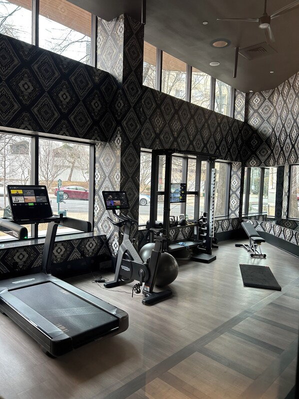 A gym with exercise equipment, large windows, and patterned walls.