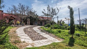 A pathway leading to a building with a stone and concrete design, surrounded by greenery and a clear sky. - Villa Sant'elene (Uri)
