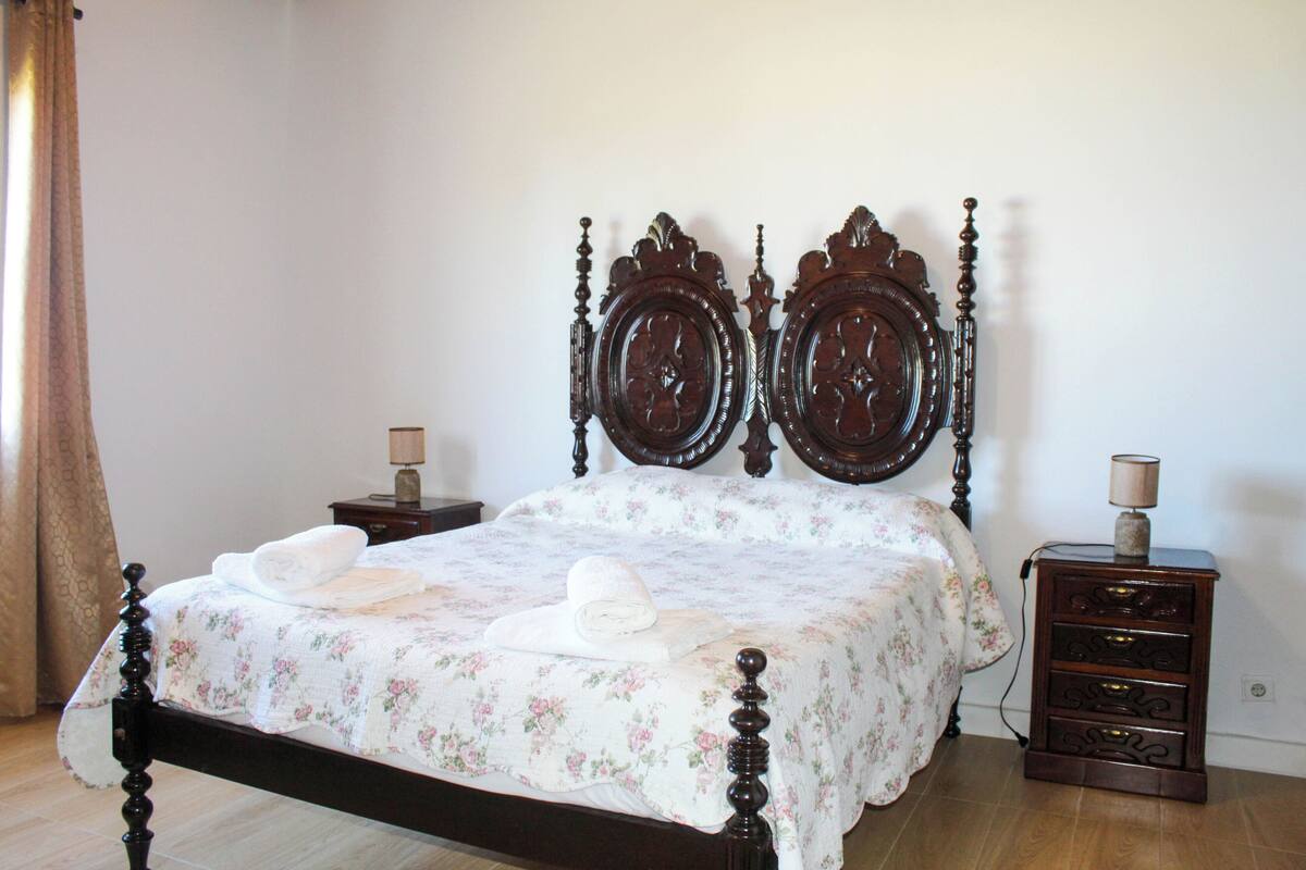 A neatly made bed with floral bedding, a wooden headboard, and a nightstand with a lamp.