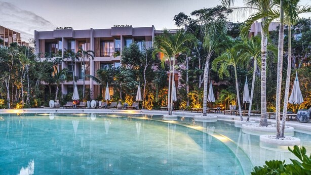 A hotel with a swimming pool, palm trees, and lounge chairs.