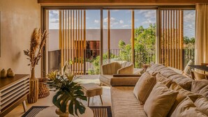 A modern living room with a sofa, a coffee table, and a large window with a view of greenery and a building.
