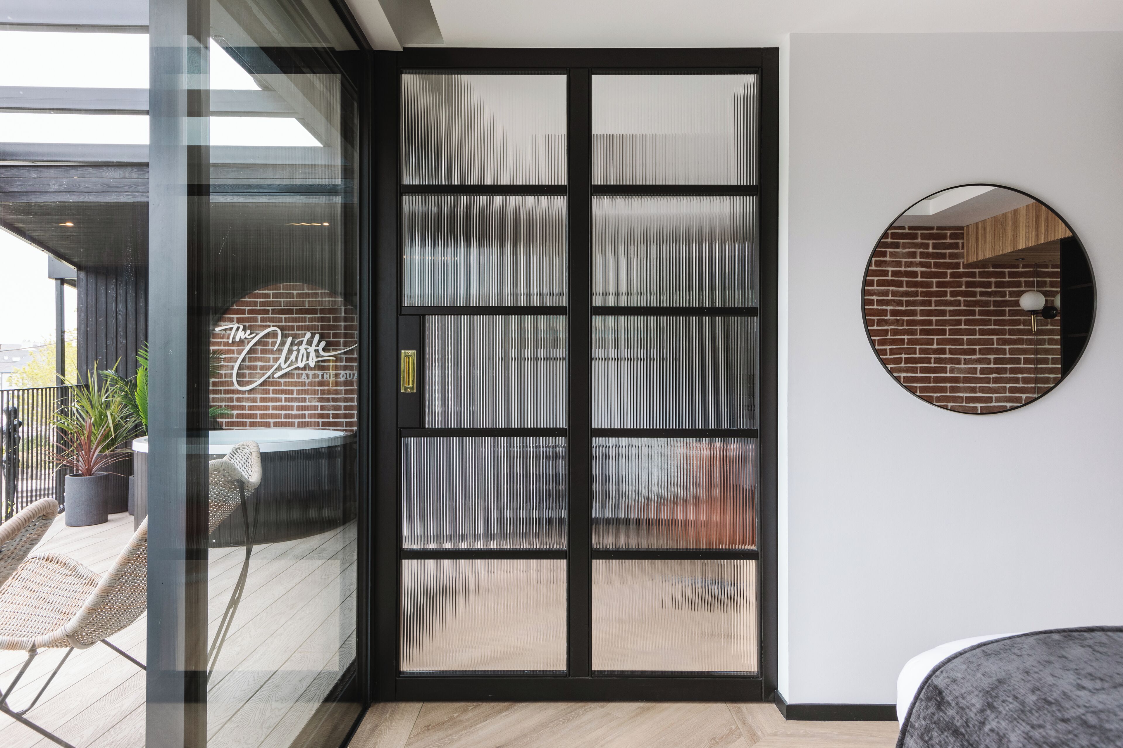 Una habitación moderna con puerta de cristal corredera que da a un espacio exterior con mobiliario de mimbre y una planta en maceta.