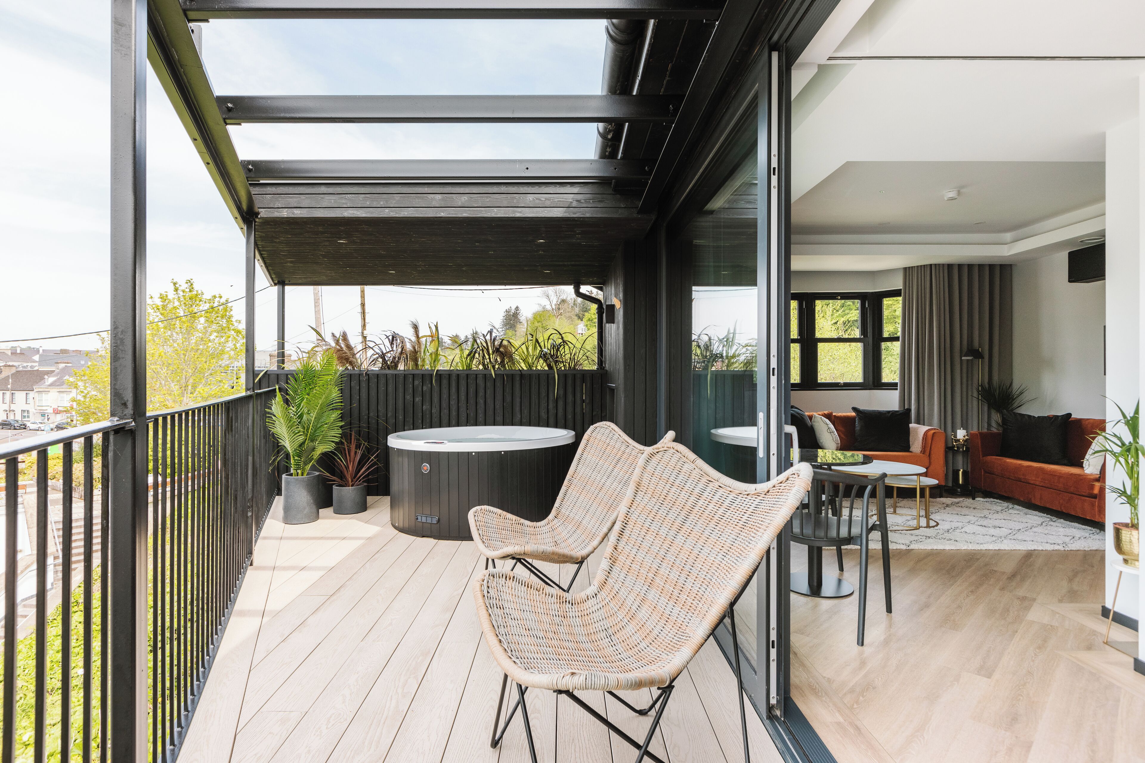 A balcony with wicker chairs, a hot tub, and a dining area with a table and chairs.