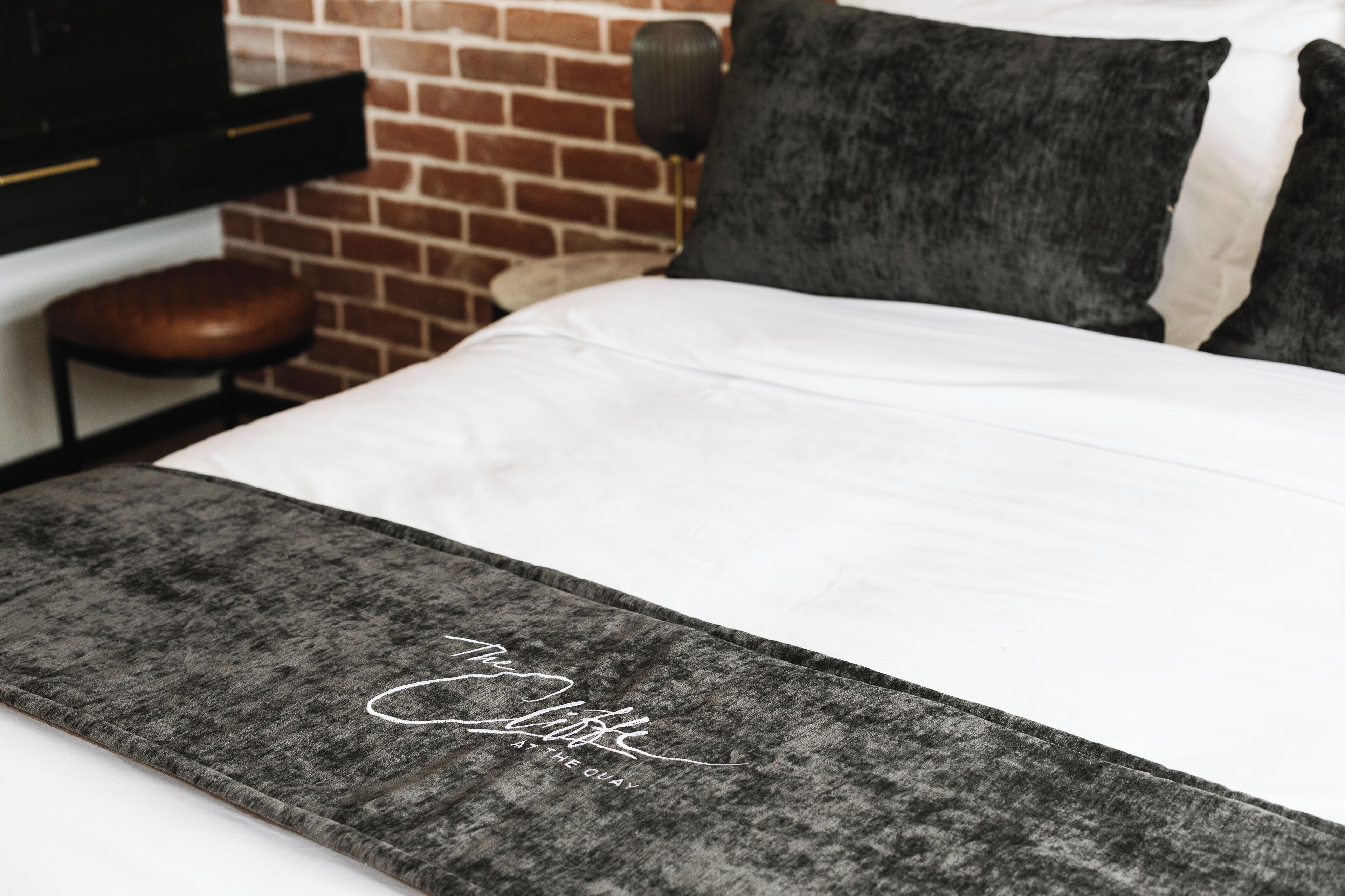 A bed with a grey and white bedspread, a black and white pillow, and a black headboard.