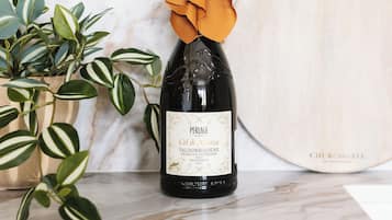 Una botella de vino con etiqueta, una tabla de madera cortadora y una planta en maceta sobre una superficie de mármol.