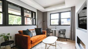 Una sala de estar moderna con un sofá, una mesa de centro y un televisor. Hay ventanas amplias y una chimenea.