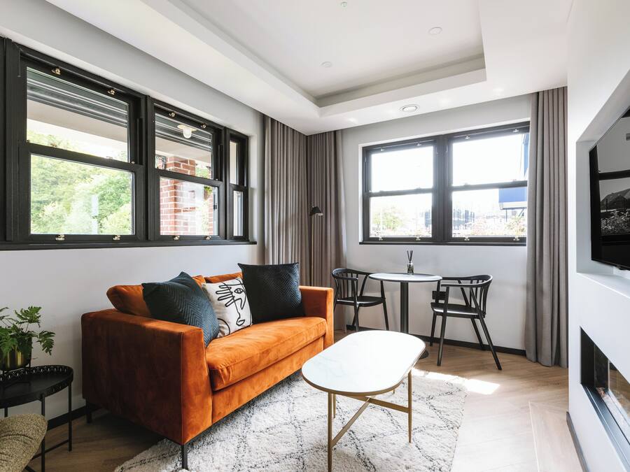 Una sala de estar moderna con un sofá, una mesa de centro y un televisor. Hay ventanas amplias y una chimenea.