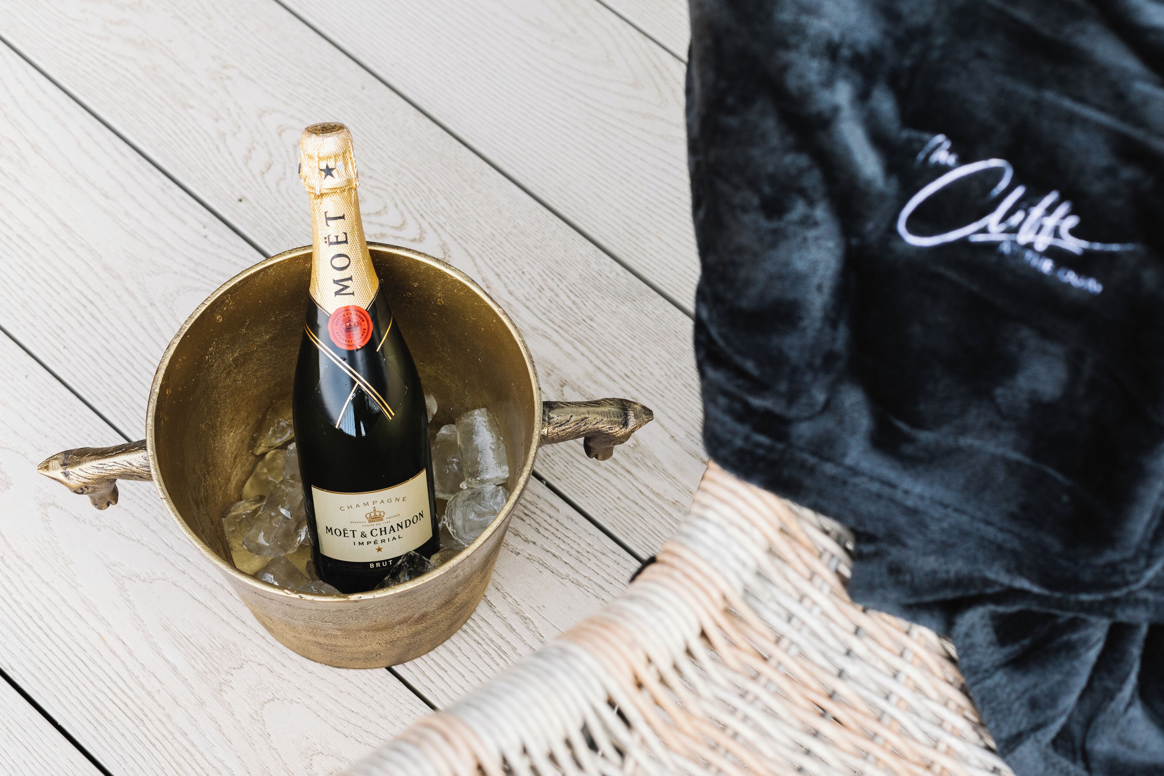 A bottle of Moët & Chandon champagne in a brass bucket with ice, placed on a wooden floor next to a black velvet bag with a logo.