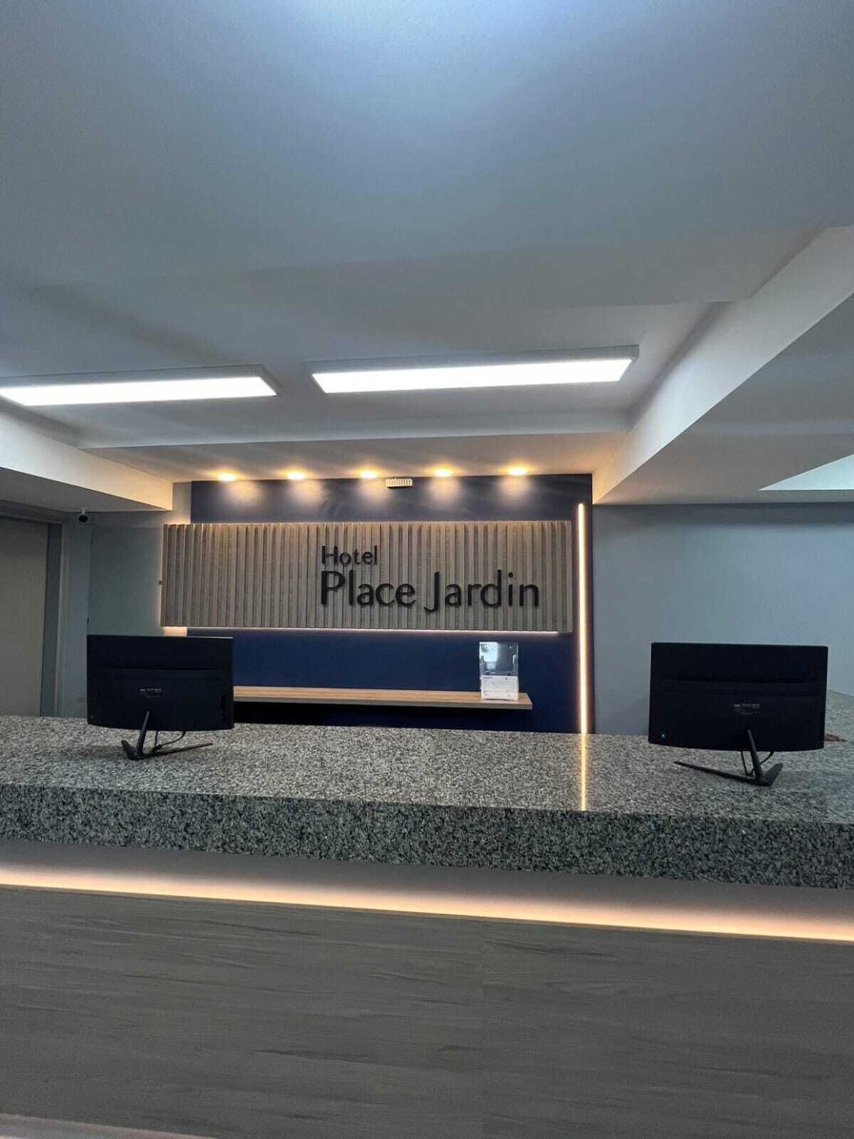 En receptionsdisk med en skylt som visar texten ”Hotel Place Jardin” och två bildskärmar på var sin sida.