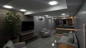A modern living room with a flat-screen TV, grey sofas, a coffee table, and a potted plant. - Hotel Place Jardin (Garanhuns)