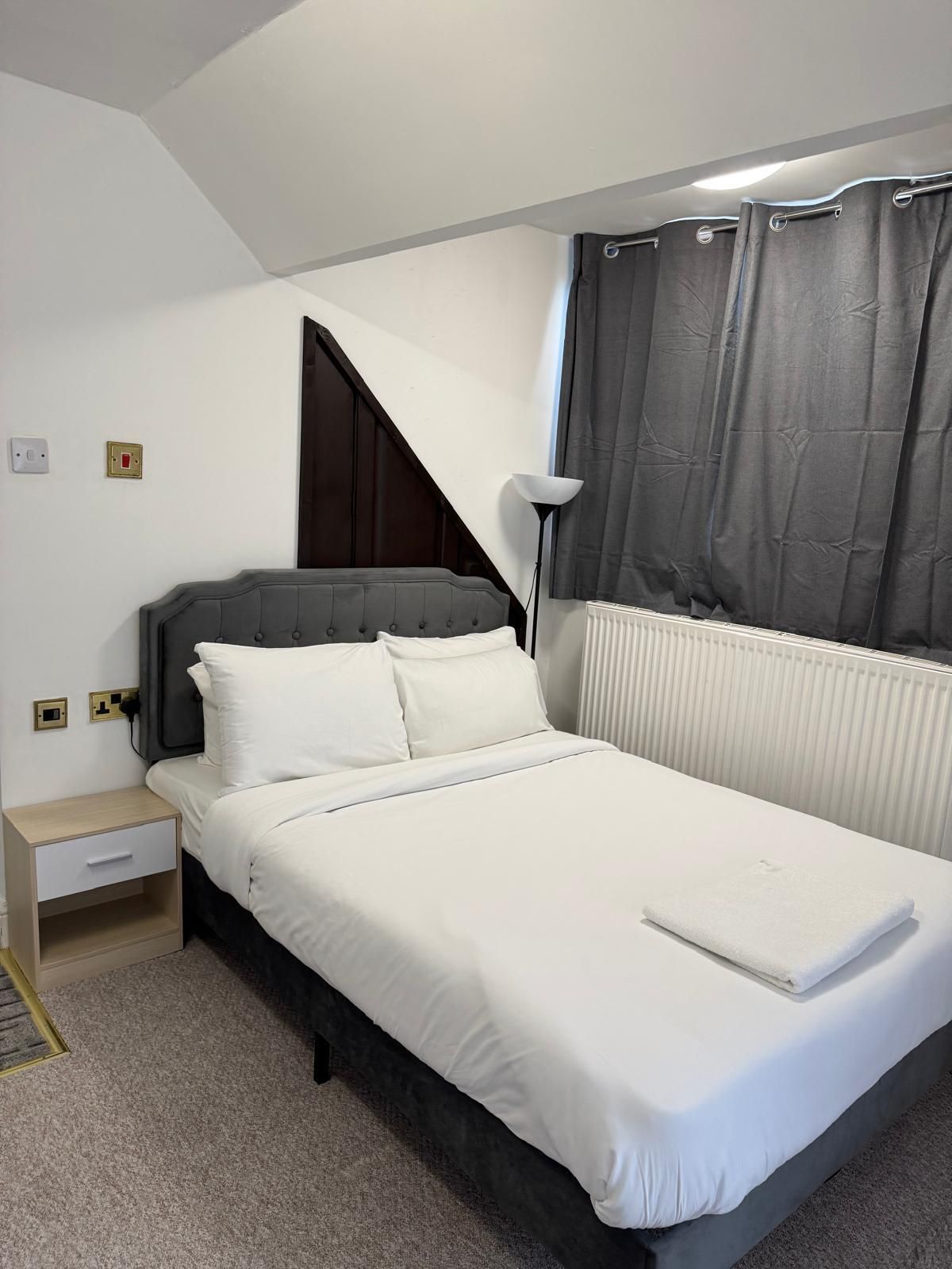A bedroom with a bed, bedside table, lamp, and a window with curtains.