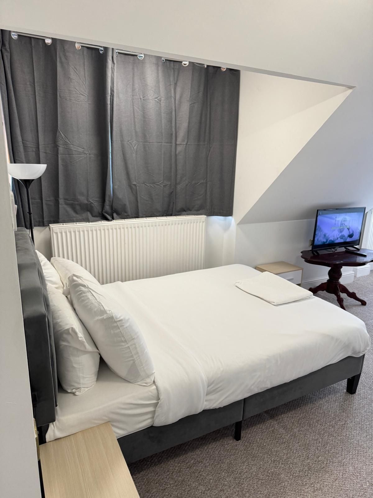 A bedroom with a bed, a nightstand, a lamp, a television, and a radiator.