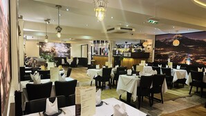 A restaurant with tables set for dining, a bar area, and a mural of a mountainous landscape. - Woodcock Inn (East Grinstead)