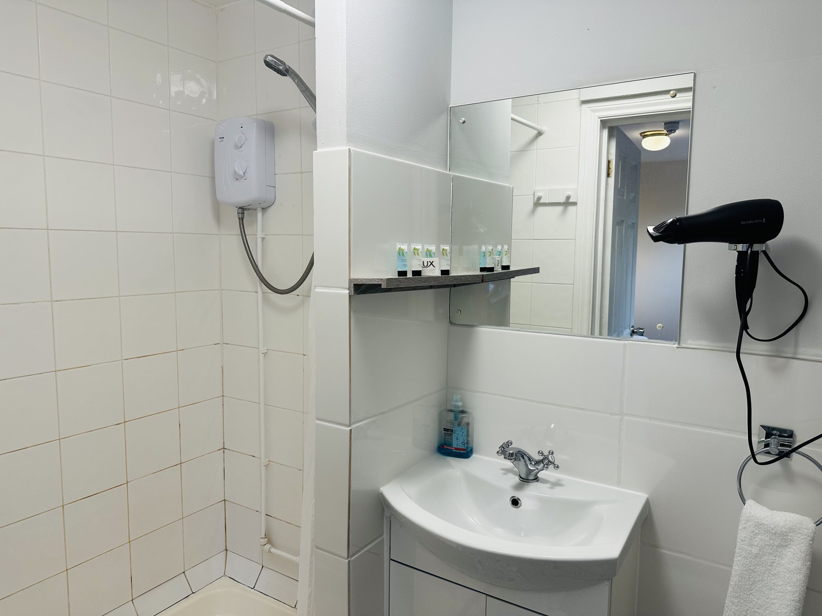 A bathroom with a shower, a sink, a mirror, and a hairdryer.