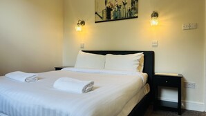 A neatly made bed with white linens and towels, a dark headboard, and a wall-mounted painting above it. - Woodcock Inn (East Grinstead)