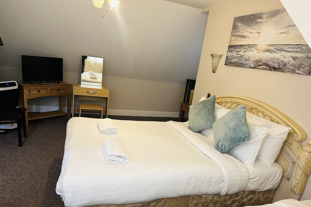 A hotel room with a bed, a desk, a chair, a television, and a painting on the wall.